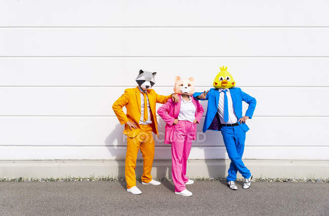 Три человека в ярких костюмах и масках животных, позирующих бок о бок перед белой стеной — стоковое фото