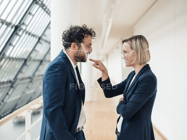 Femme d'affaires souriante avec masque pointant vers un collègue au bureau — Photo de stock