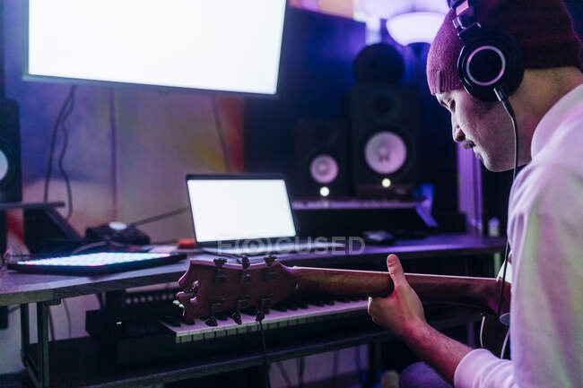Homme portant un casque jouant de la guitare au home studio — Photo de stock