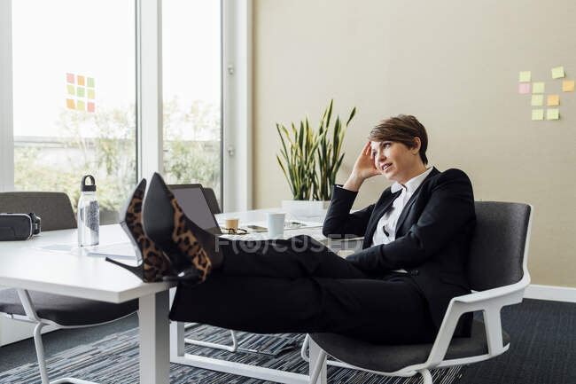 Жінка-професіонал з головою в руках, дивлячись далеко, сидячи за столом в офісі — стокове фото