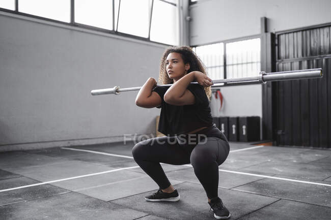 Lockige junge Frau übt Kniebeugen im Fitnessstudio — Stockfoto