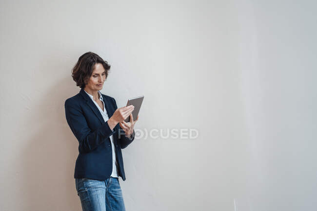 Femme utilisant une tablette numérique tout en s'appuyant sur un mur blanc — Photo de stock