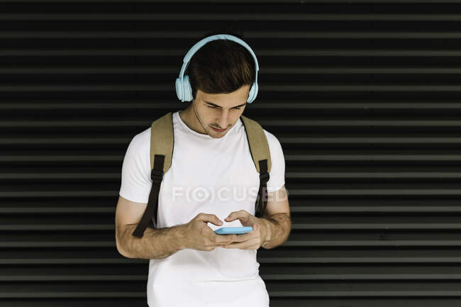 Hombre usando auriculares usando teléfono inteligente en frente del obturador - foto de stock