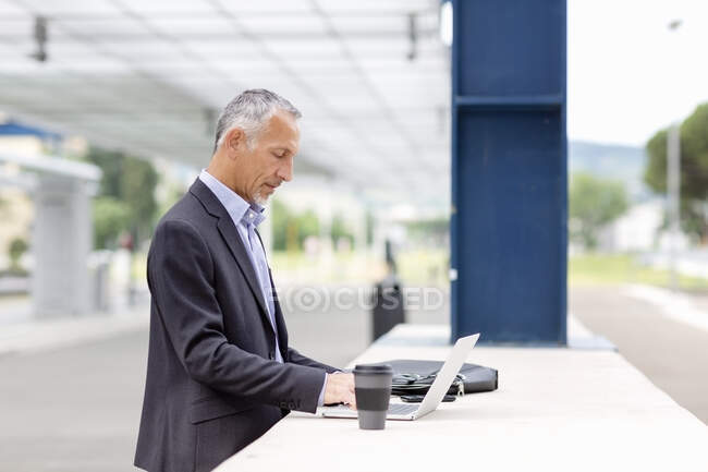 Professionista maschile che lavora su laptop alla stazione ferroviaria — Foto stock