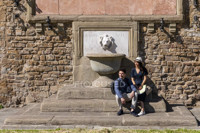 Lächelndes Paar sitzt an sonnigem Tag vor Brunnen — Stockfoto