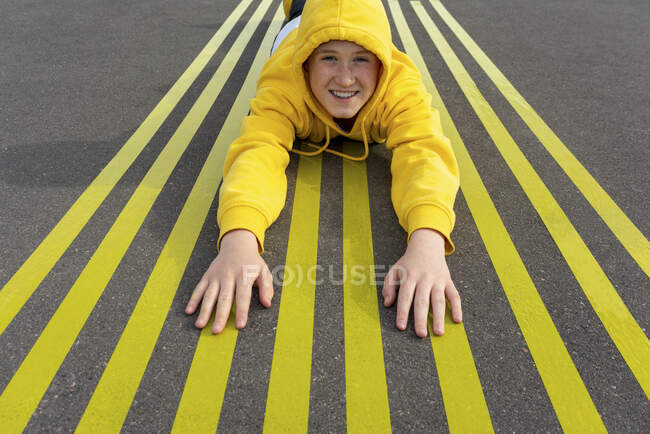 Ragazzo sorridente sdraiato su strisce marcature stradali gialle — Foto stock