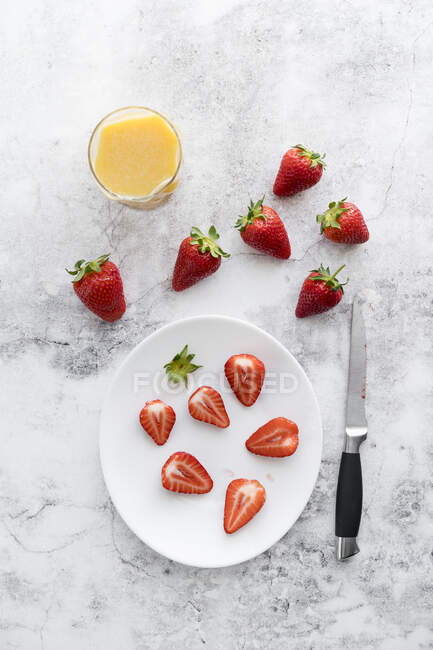 Verre de jus d'orange, couteau de cuisine et assiette aux fraises fraîches couchées sur marbre blanc — Photo de stock