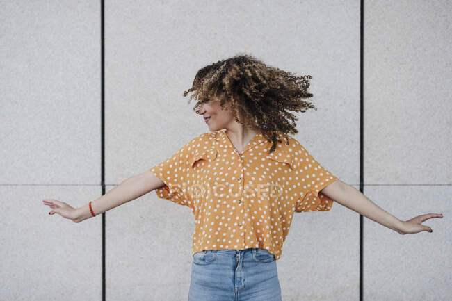 Giovane donna con le braccia tese gettando i capelli davanti al muro — Foto stock