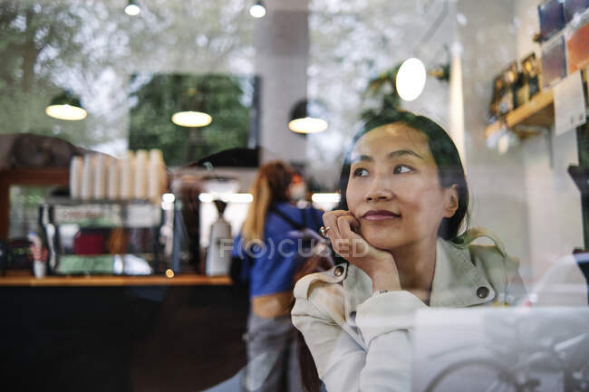 Mujer adulta con portátil contemplando mientras está sentado en la cafetería - foto de stock