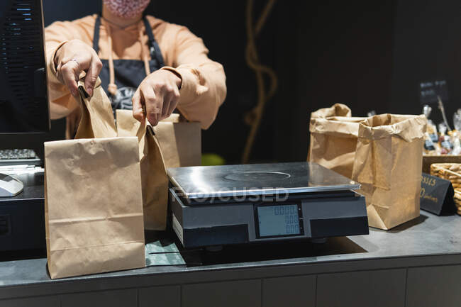 Propietaria de una tienda de comestibles manteniendo la bolsa de comestibles en escala de peso - foto de stock