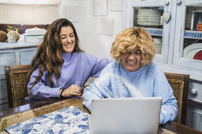 Mutter und Tochter lächeln beim Blick auf Laptop in Küche — Stockfoto