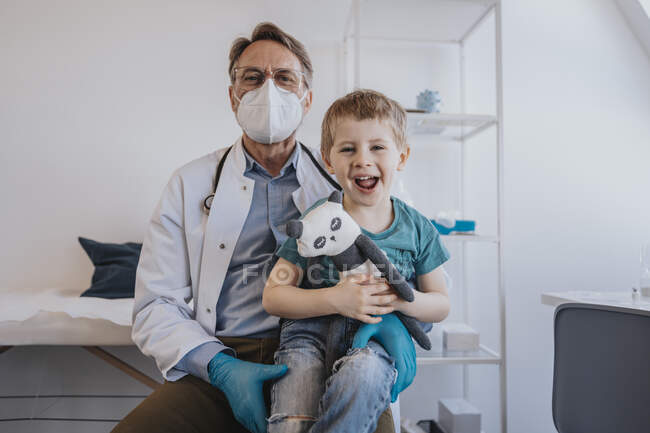 Ragazzo allegro ridere mentre seduto sulle ginocchia del medico in sala visite mediche — Foto stock