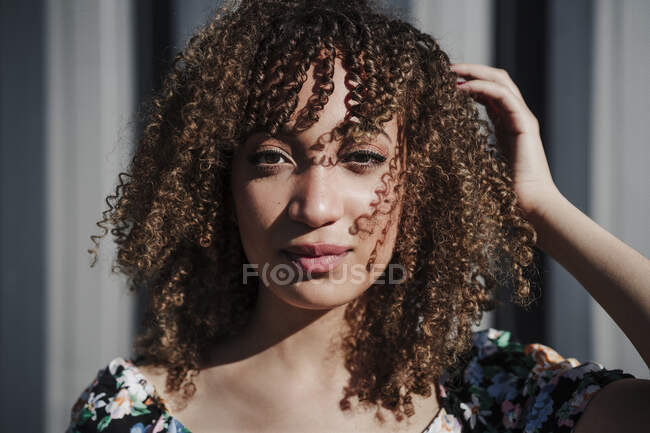 Jovem de cabelos encaracolados mulher de pé com a mão no cabelo durante o dia ensolarado — Fotografia de Stock