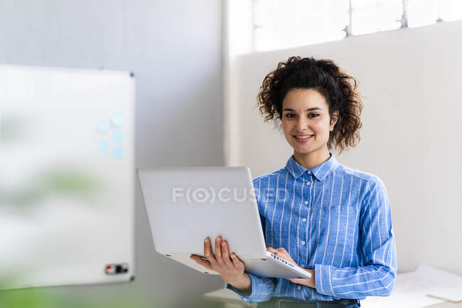 Жіночий підприємець тримає ноутбук, стоячи у творчому кабінеті. — стокове фото