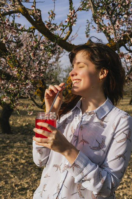 Mujer sonriente tomando refrescos de fresa en almendros - foto de stock