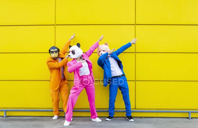 Três adultos vestindo trajes vibrantes e máscaras de animais se unindo na frente da parede amarela — Fotografia de Stock
