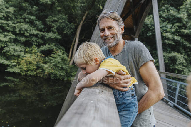 Smiling man carrying son leaning over railing — Stock Photo