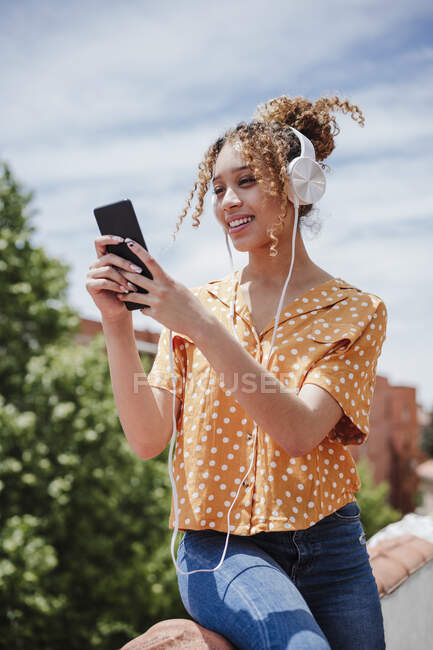 Mujer tomando selfie en el teléfono inteligente mientras escucha música en el balcón - foto de stock