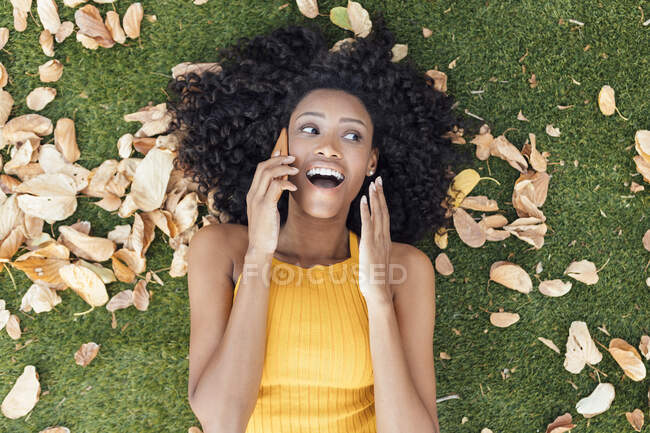 Donna sorpresa che parla su smart phone mentre giace sull'erba al parco — Foto stock
