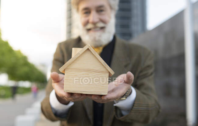 Smiling mature salesman showing wooden model house — Stock Photo