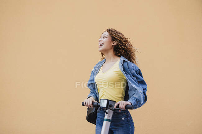 Donna allegra con scooter elettrico a spinta da parete beige — Foto stock