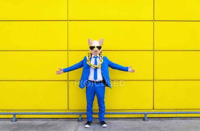 Чоловік у яскравому синьому костюмі, маска свині і великий золотий ланцюжок, що стоїть перед жовтою стіною з розкритими руками. — стокове фото