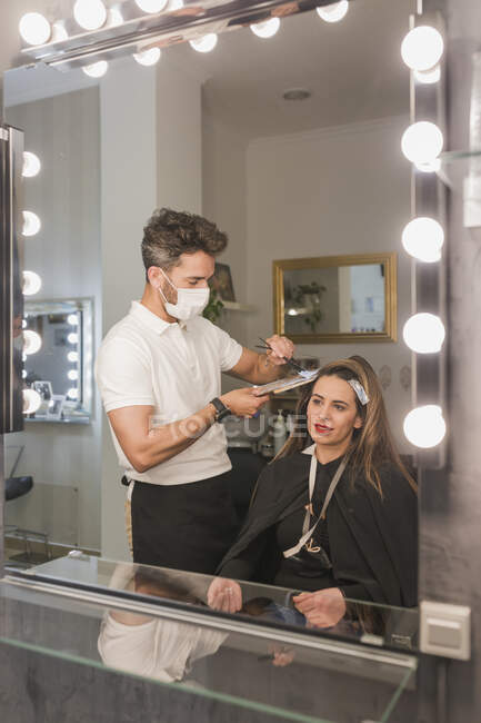 Дзеркало дзеркала чоловіка, який фарбує жіноче волосся клієнта в салоні — стокове фото
