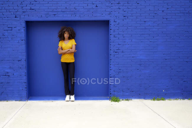 Afro donna con le braccia incrociate in piedi sul sentiero davanti al muro di mattoni blu — Foto stock
