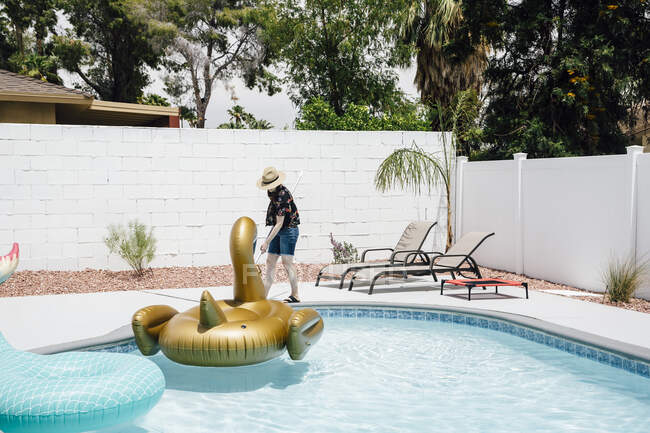 Frau mit Hut putzt Schwimmbad im Urlaub mit Stange — Stockfoto