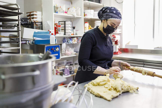 Fêmea padeiro com rolo e massa na cozinha comercial na padaria — Fotografia de Stock