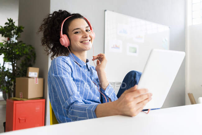 Smiling female entrepreneur with headphones and digital tablet in office — Stock Photo