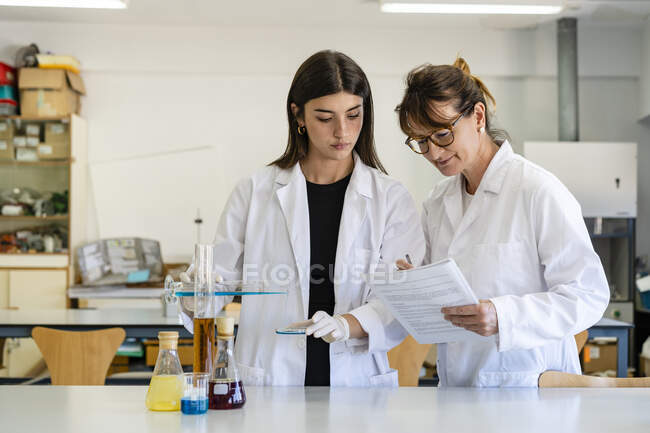 Женщина-ученый читает документ, помогая коллеге экспериментировать в лаборатории — стоковое фото