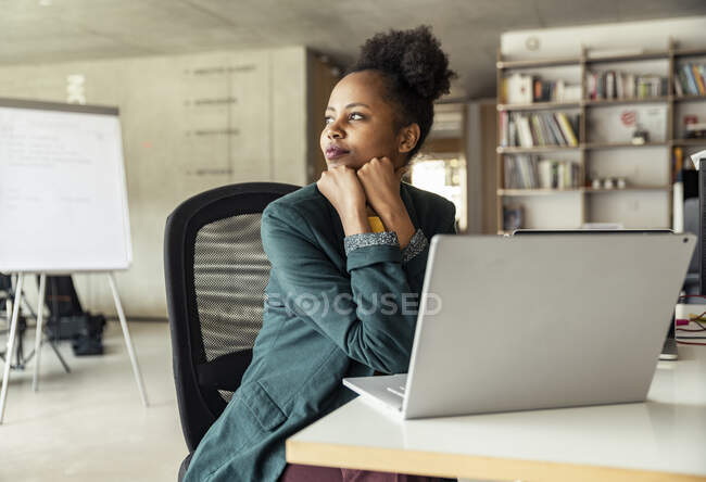Unternehmerin mit der Hand am Kinn träumt am Schreibtisch — Stockfoto