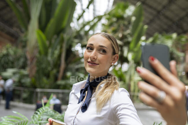 Jeune hôtesse de l'air prenant selfie sur téléphone intelligent dans le jardin du café — Photo de stock