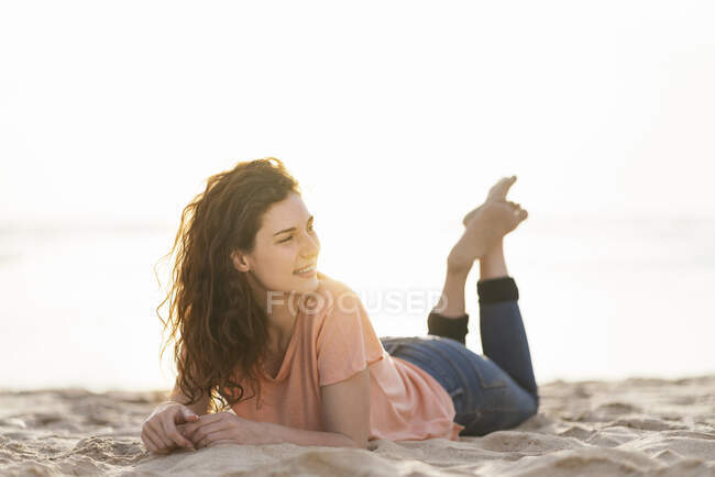 Young woman looking away while lying on sand during sunny day — Stock Photo