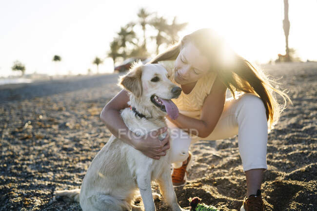 Femme souriante embrassant le chien sur le sable pendant la journée ensoleillée le week-end — Photo de stock
