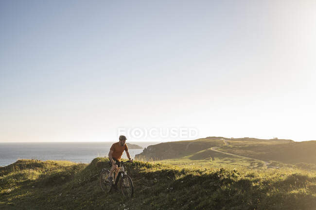 Hombre atleta ciclismo en la hierba cerca del mar al atardecer - foto de stock