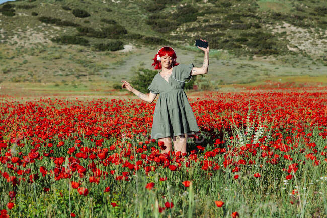 Junge Frau mit Smartphone tanzt bei sonnigem Wetter auf Mohnfeld — Stockfoto