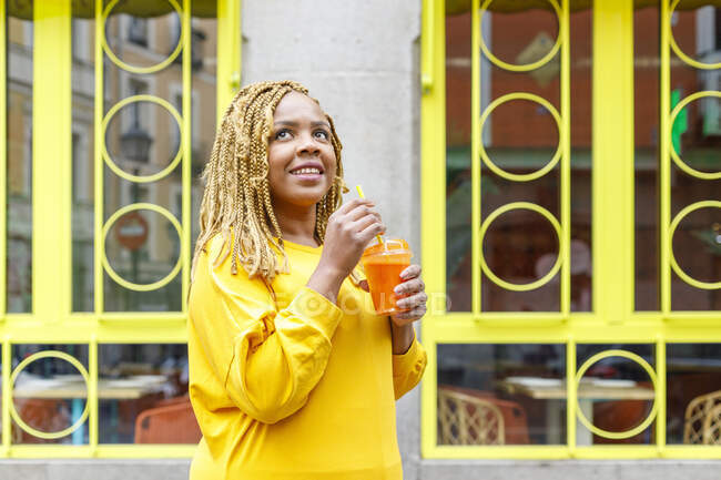 Mujer sonriente sosteniendo el jugo mientras mira hacia arriba y sueña de día - foto de stock