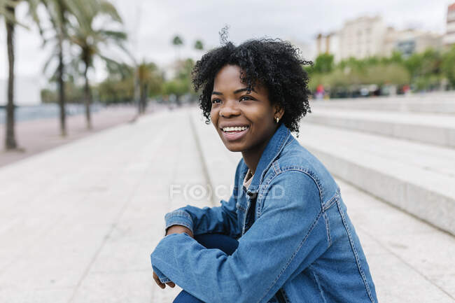 Afro junge Frau schaut weg, während sie auf Stufen sitzt — Stockfoto