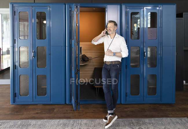 Businessman talking at telephone booth in office — Stock Photo