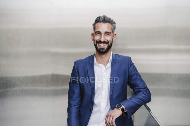 Mid adult businessman smiling while leaning on railing in front of silver colored wall — Stock Photo