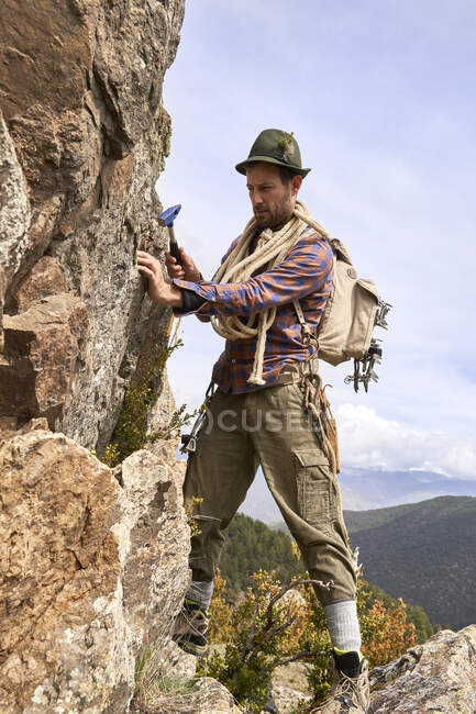 Male tourist with backpack and hammer standing by rock on mountain — Stock Photo
