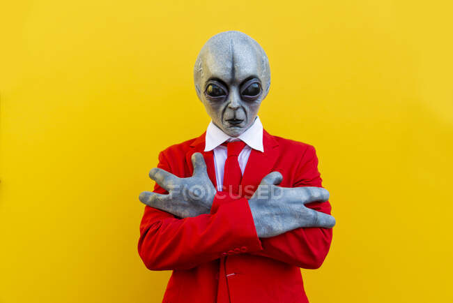 Retrato del hombre con traje alienígena y traje rojo brillante de pie con los brazos cruzados - foto de stock