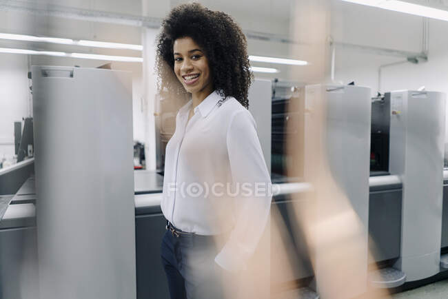 Smiling businesswoman standing by machines in industry — Stock Photo