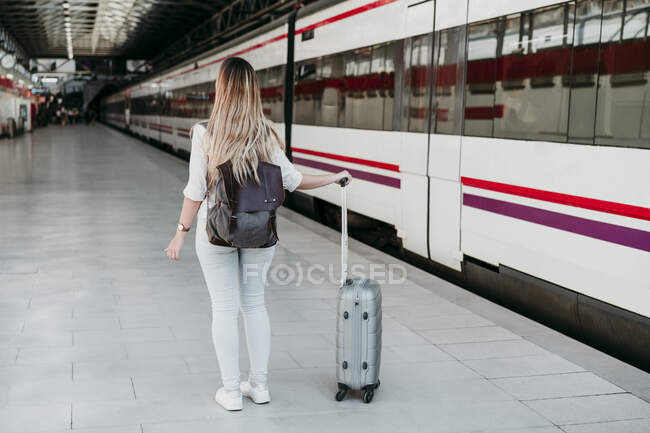 Jovem passageira vestindo mochila de pé com bagagem de rodas na plataforma da estação ferroviária — Fotografia de Stock