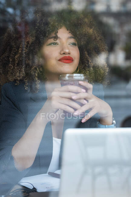 Bella donna d'affari che sogna mentre tiene il caffè ghiacciato davanti al computer portatile al caffè — Foto stock