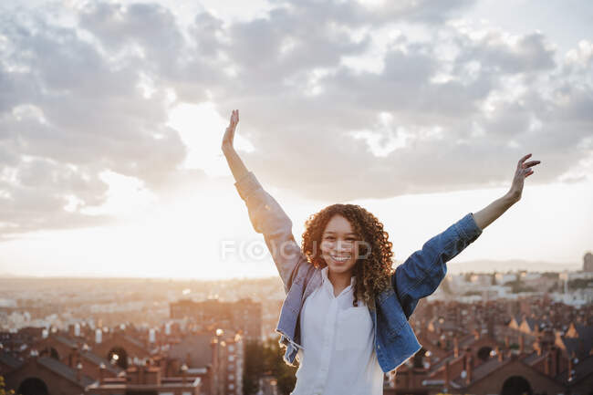 Donna sorridente con le braccia alzate davanti alla città — Foto stock