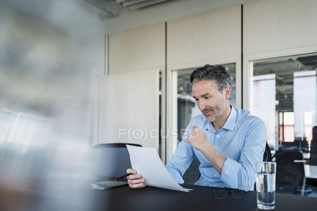 Documentos de lectura profesional masculina mientras está sentado en el escritorio en la oficina - foto de stock