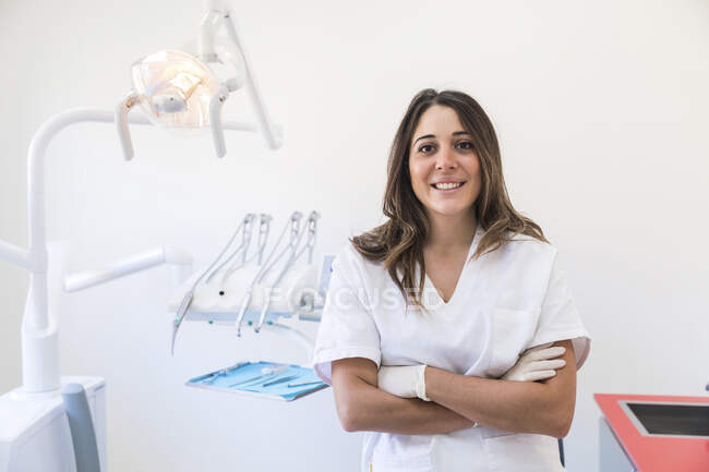 Dentista sonriente con los brazos cruzados en la clínica médica - foto de stock